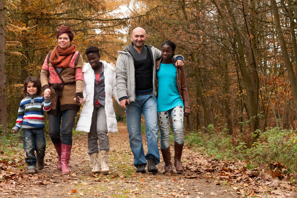 a multiracial family linking arms and walking in a fall forest