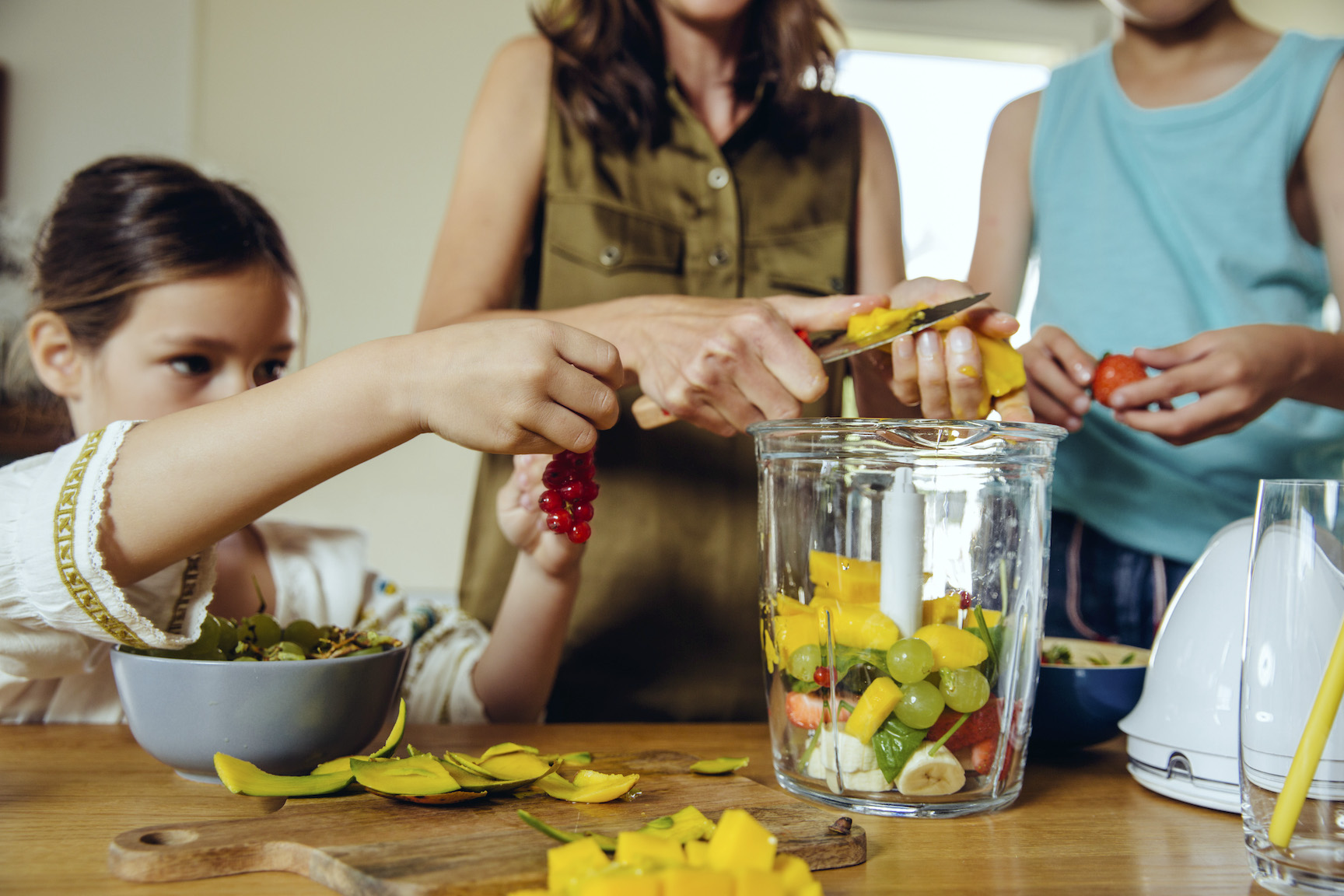 Mother and children putting fruit into a smoothie blender; blended family parenting dynamics