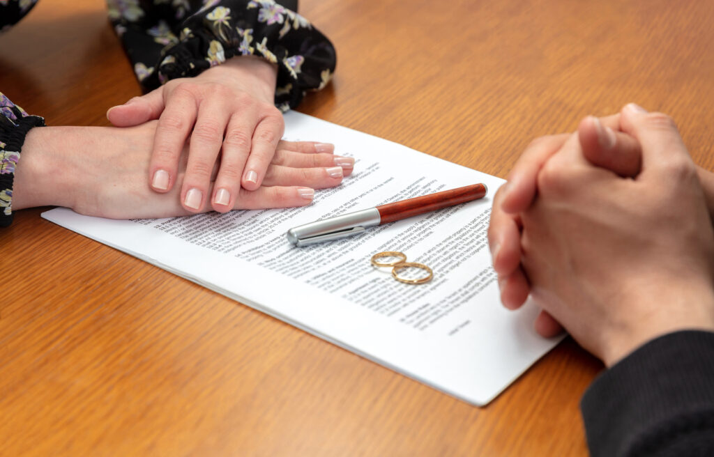 Divorce agreement, marriage dissolution documents. Man and woman hands, wedding rings and legal papers for signature on a wooden table, lawyer office