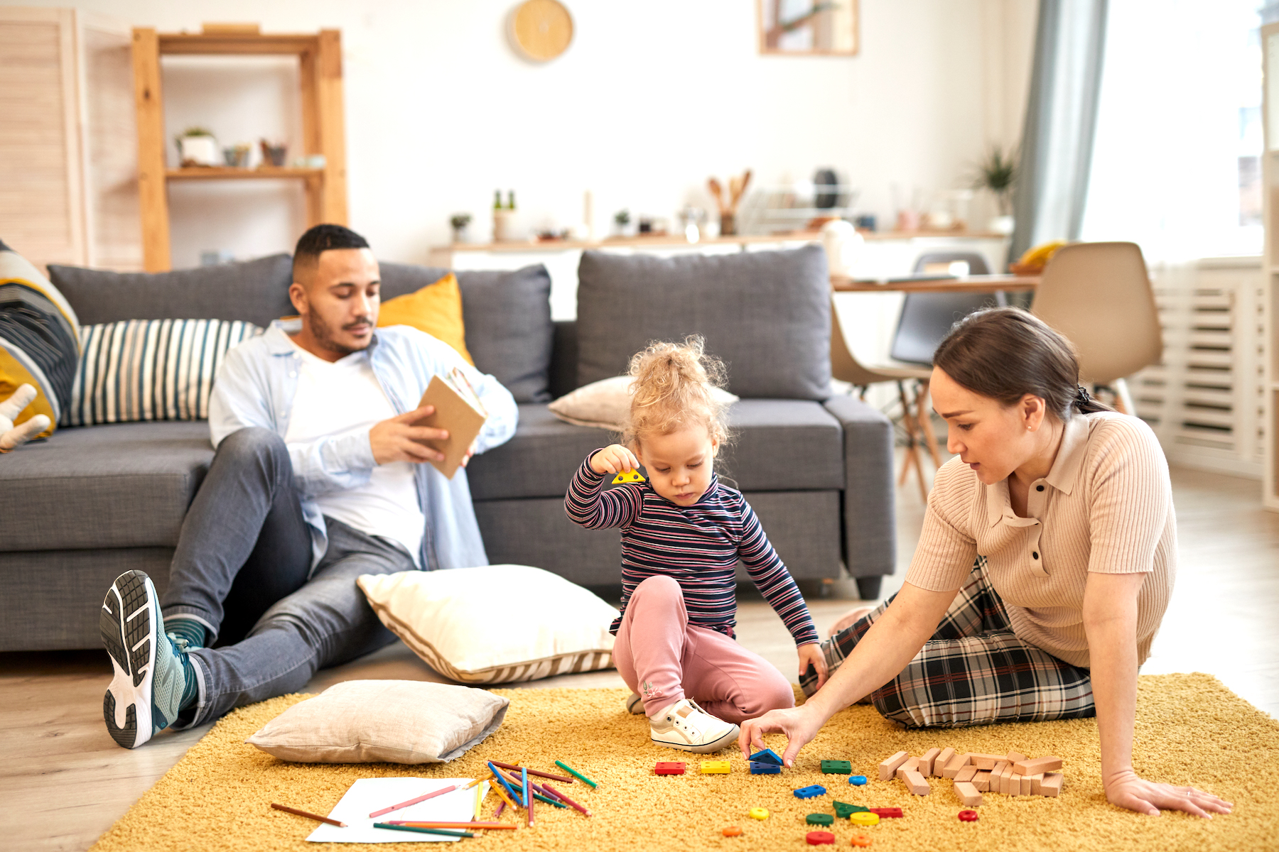 Full length portrait of modern mixed-race family playing with cute little girl in cozy living room interior