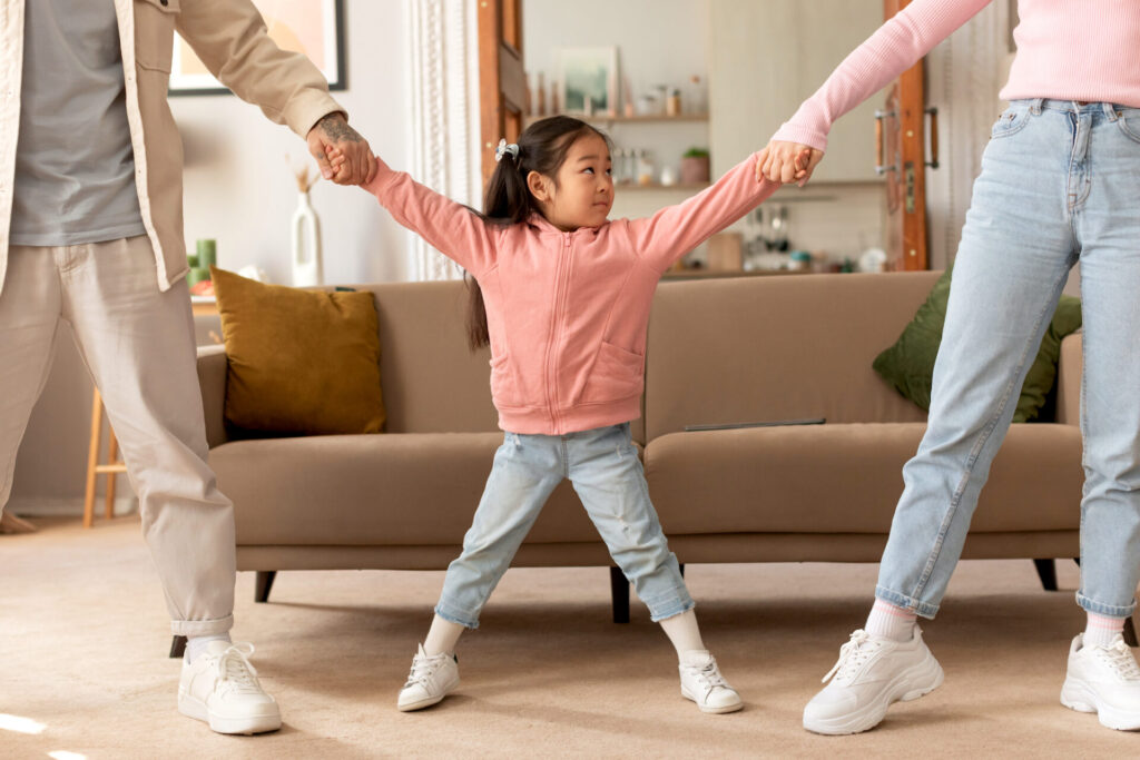 Asian parents pulling daughter's hands in different directions standing indoor